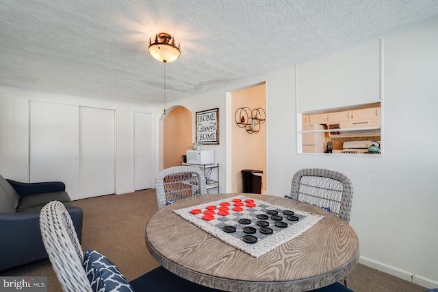 dining room featuring a decorative wall, carpet, arched walkways, and a textured ceiling