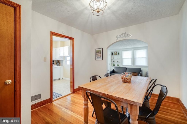 dining area with baseboards, visible vents, arched walkways, light wood-style floors, and a textured ceiling