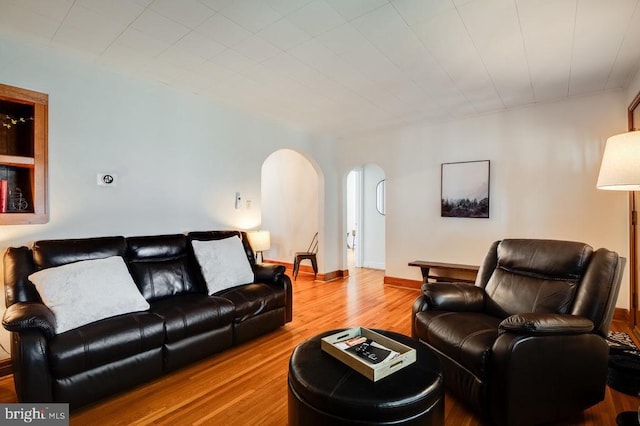 living room featuring wood finished floors, arched walkways, and baseboards