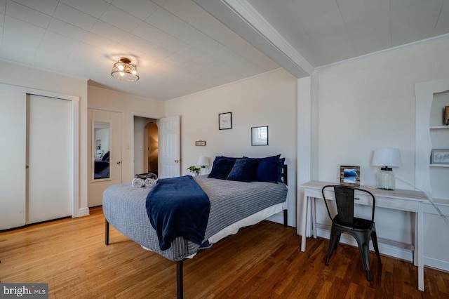 bedroom with wood finished floors, arched walkways, and ornamental molding