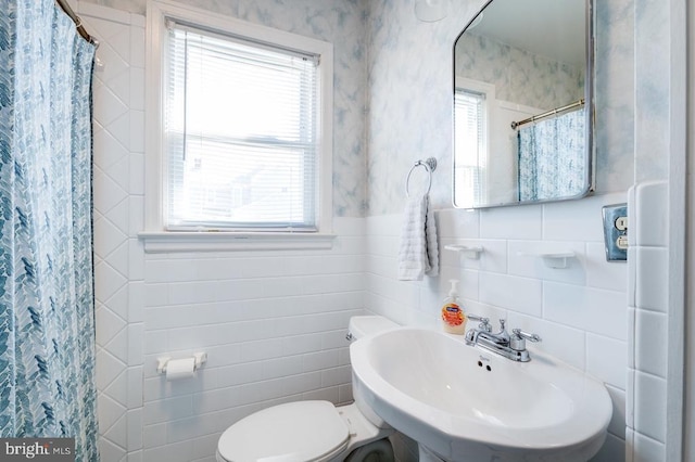 bathroom featuring a shower with curtain, toilet, a sink, tile walls, and wallpapered walls