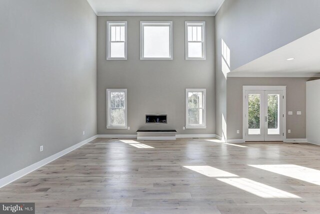 unfurnished living room with french doors, ornamental molding, a towering ceiling, and light hardwood / wood-style flooring