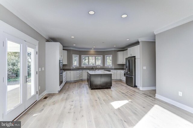 kitchen featuring sink, stainless steel refrigerator, a kitchen island, a healthy amount of sunlight, and white cabinets