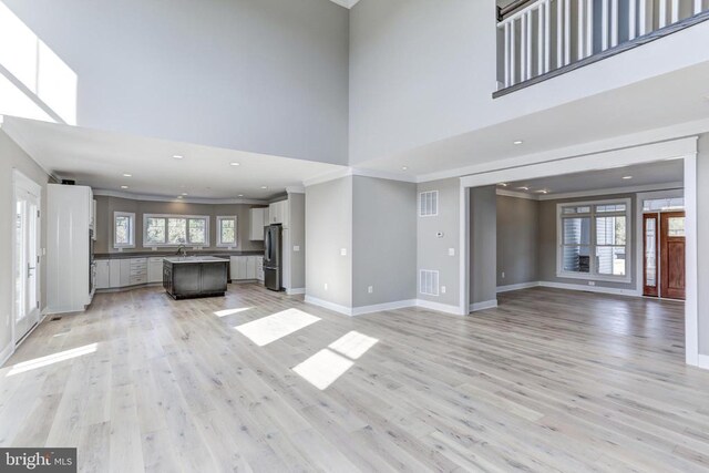 unfurnished living room featuring crown molding, a wealth of natural light, light hardwood / wood-style flooring, and a towering ceiling