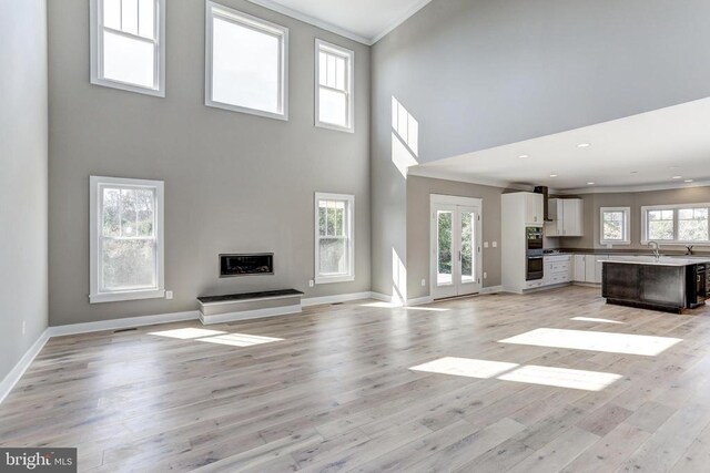 unfurnished living room with a high ceiling, ornamental molding, light hardwood / wood-style floors, and french doors