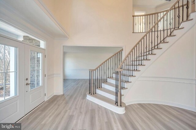 foyer with french doors, plenty of natural light, crown molding, and light wood-type flooring