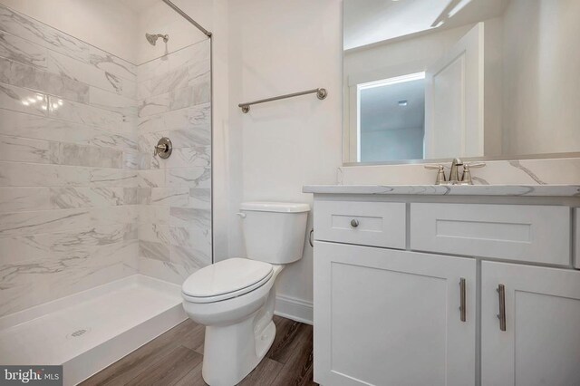 bathroom with tiled shower, wood-type flooring, toilet, and vanity