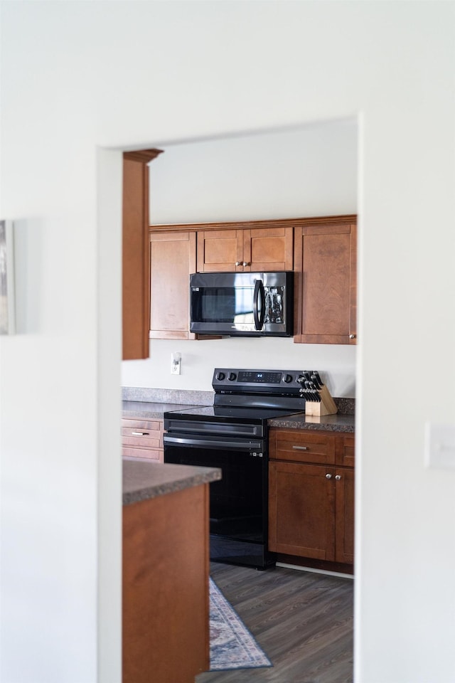 kitchen with dark countertops, dark wood-style floors, brown cabinetry, and black range with electric stovetop