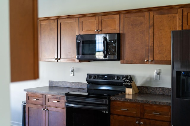 kitchen with dark countertops, black electric range, brown cabinetry, and stainless steel refrigerator with ice dispenser