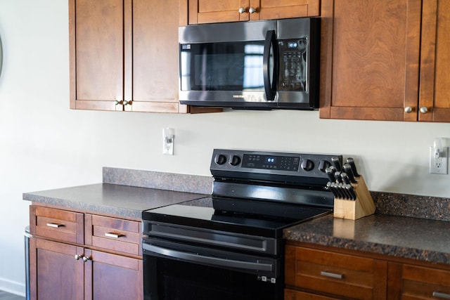 kitchen featuring dark countertops, stainless steel microwave, brown cabinets, and electric stove