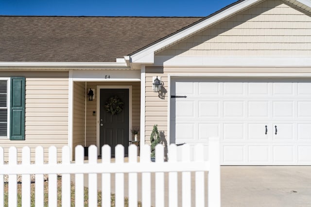 view of exterior entry with concrete driveway, a garage, and roof with shingles