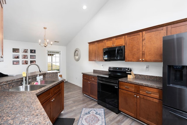 kitchen with dark countertops, light wood-style floors, brown cabinetry, black appliances, and a sink