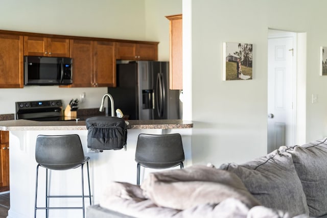 kitchen featuring dark countertops, a breakfast bar, brown cabinetry, black appliances, and a sink