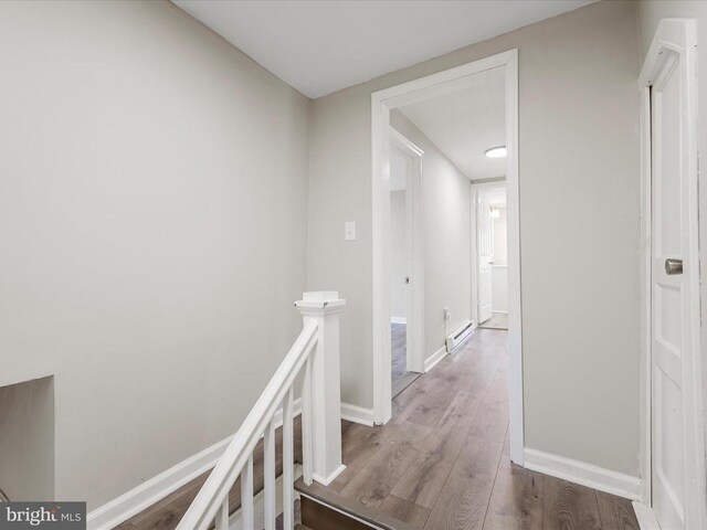 corridor with a baseboard heating unit and hardwood / wood-style floors