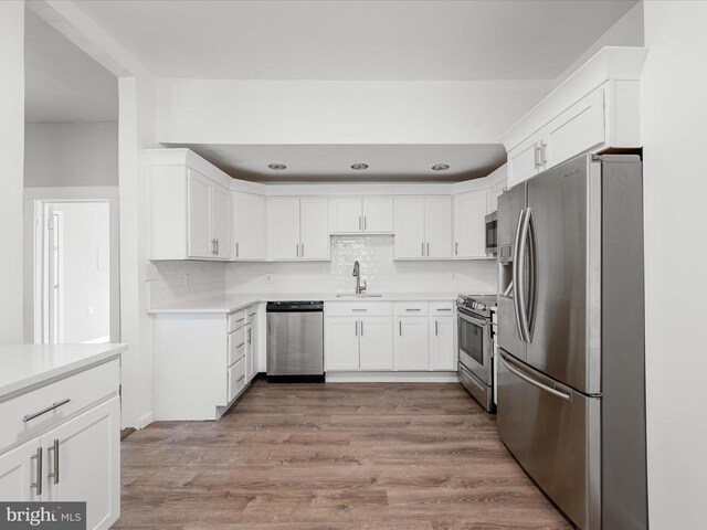 kitchen with sink, backsplash, white cabinets, stainless steel appliances, and light wood-type flooring