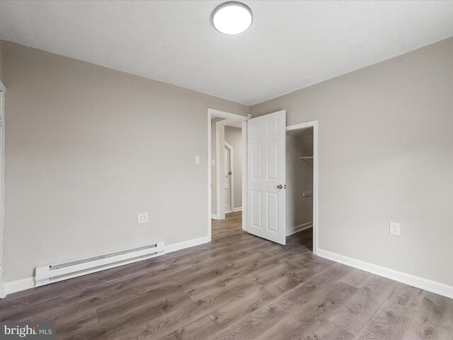 unfurnished bedroom featuring hardwood / wood-style floors, a baseboard radiator, and a closet