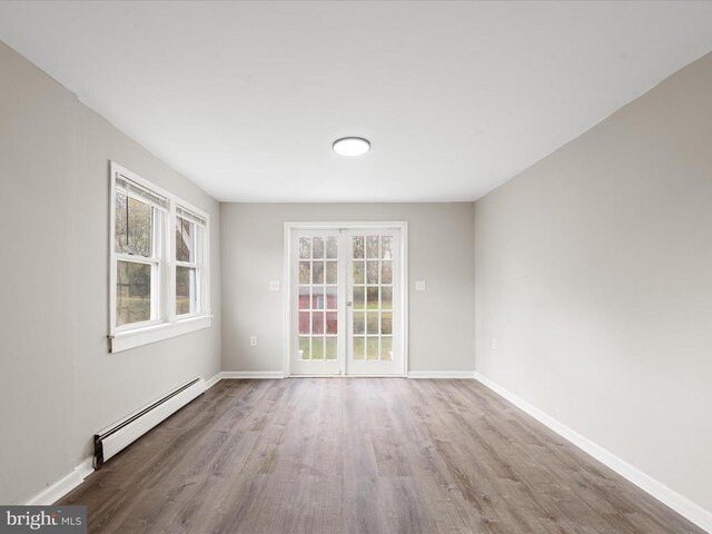 spare room with a healthy amount of sunlight, light hardwood / wood-style floors, and a baseboard heating unit