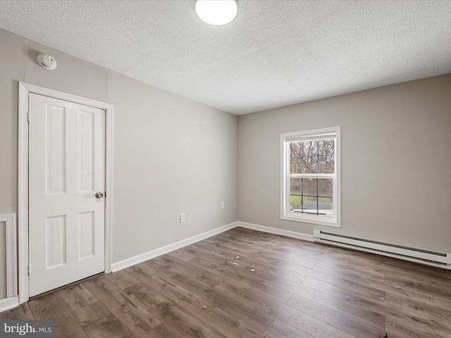 unfurnished room featuring baseboard heating, dark hardwood / wood-style floors, and a textured ceiling