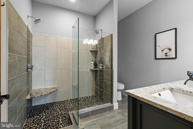 bathroom featuring tile patterned flooring, vanity, a tile shower, and toilet