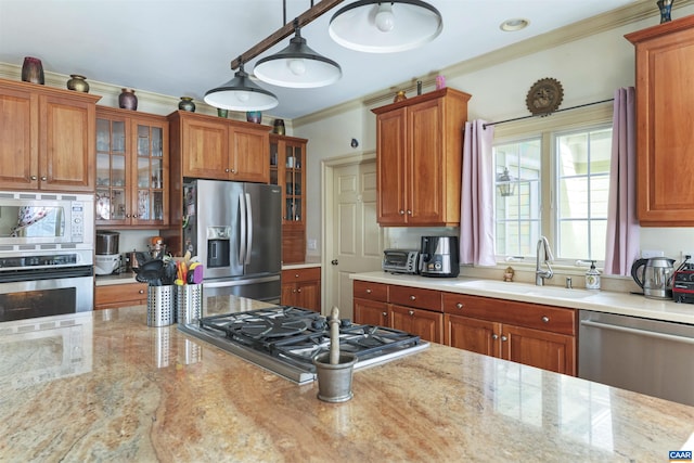 kitchen featuring ornamental molding, a sink, appliances with stainless steel finishes, brown cabinetry, and light stone countertops