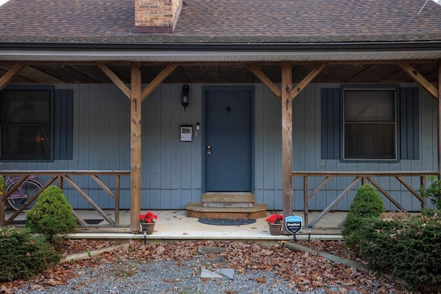 doorway to property with a porch, a shingled roof, and a chimney