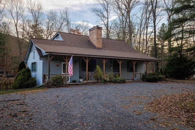 farmhouse inspired home with a chimney, gravel driveway, roof with shingles, and covered porch