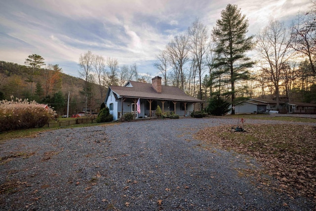 view of front of house featuring a porch, a chimney, fence, and gravel driveway