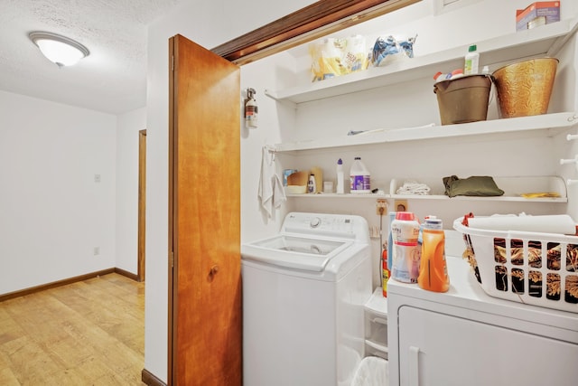 laundry room featuring laundry area, light wood-type flooring, baseboards, separate washer and dryer, and a textured ceiling