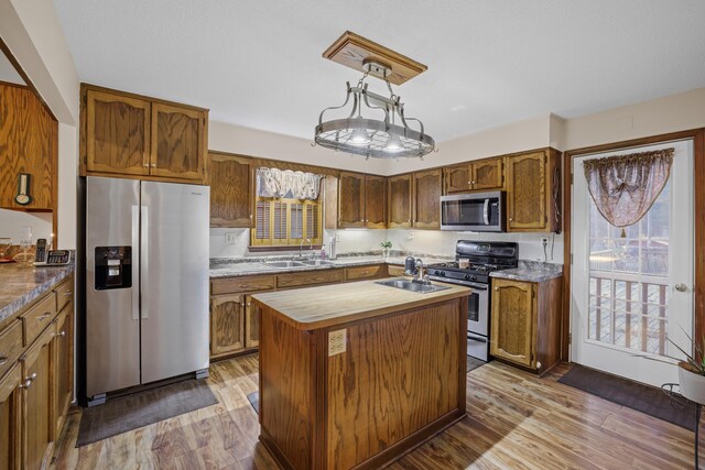 kitchen with wood finished floors, a sink, brown cabinets, an island with sink, and appliances with stainless steel finishes