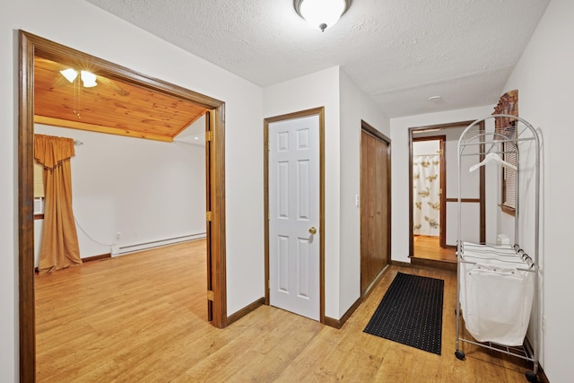 corridor with baseboard heating, baseboards, a textured ceiling, and light wood-style floors