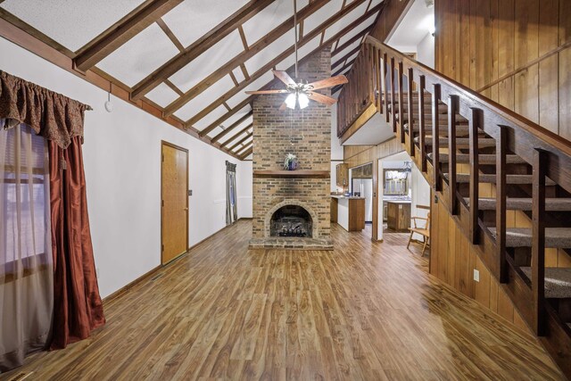 unfurnished living room with wood finished floors, stairs, beam ceiling, a fireplace, and high vaulted ceiling