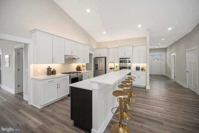 kitchen featuring appliances with stainless steel finishes, white cabinetry, a center island with sink, a kitchen bar, and decorative backsplash