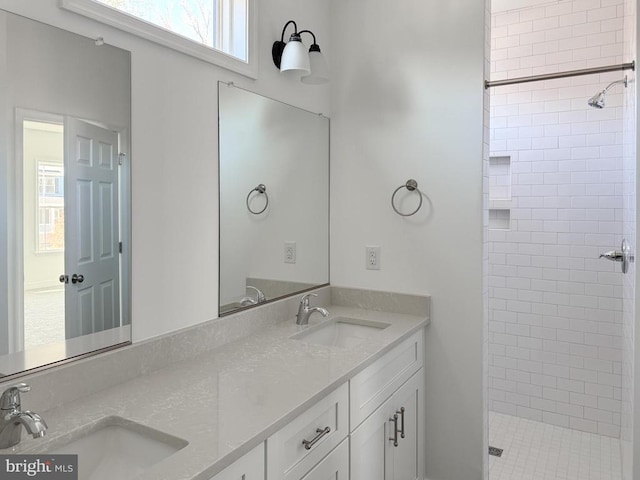 bathroom featuring a tile shower, double vanity, and a sink