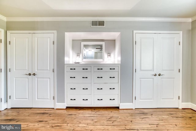 unfurnished bedroom with crown molding, multiple closets, and light wood-type flooring