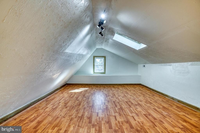 additional living space with vaulted ceiling with skylight, wood finished floors, baseboards, and a textured ceiling