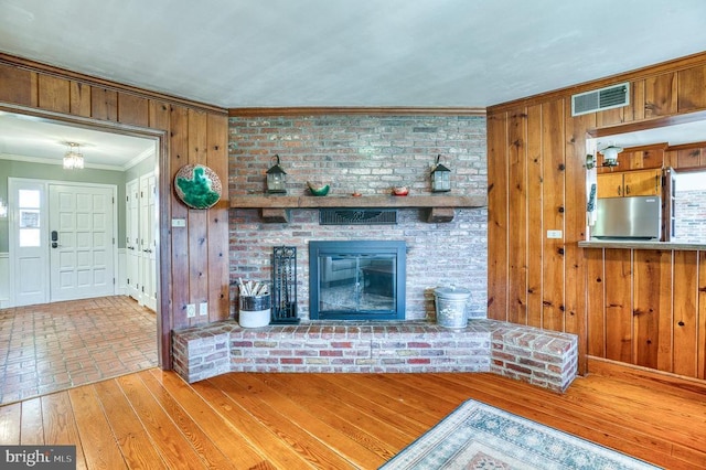 unfurnished living room with visible vents, ornamental molding, hardwood / wood-style flooring, wooden walls, and a fireplace