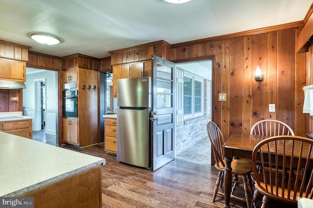 kitchen with wooden walls, black oven, light countertops, freestanding refrigerator, and dark wood-style flooring