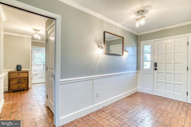 entryway featuring brick floor, wainscoting, and crown molding