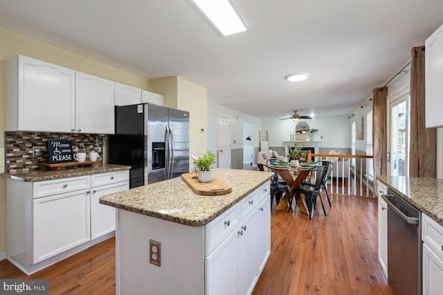 kitchen with light stone counters, decorative backsplash, appliances with stainless steel finishes, light wood-style floors, and white cabinets