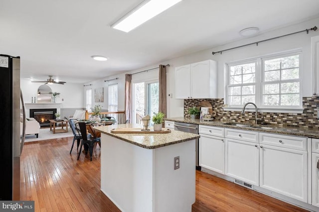 kitchen featuring a kitchen island, a glass covered fireplace, white cabinets, stainless steel appliances, and a sink