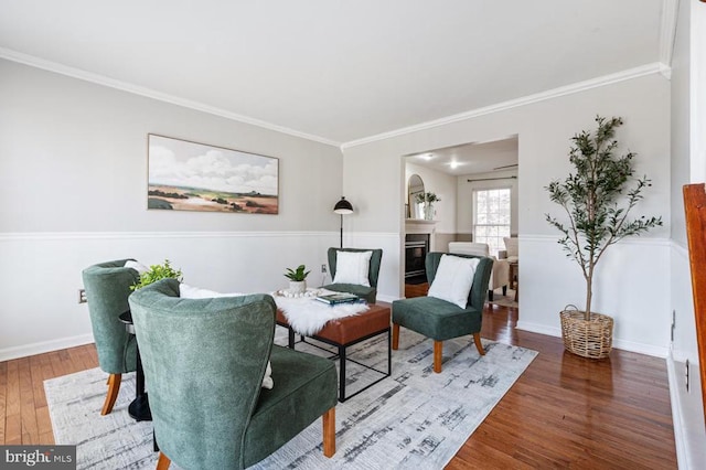 sitting room with wood finished floors, a fireplace, baseboards, and ornamental molding