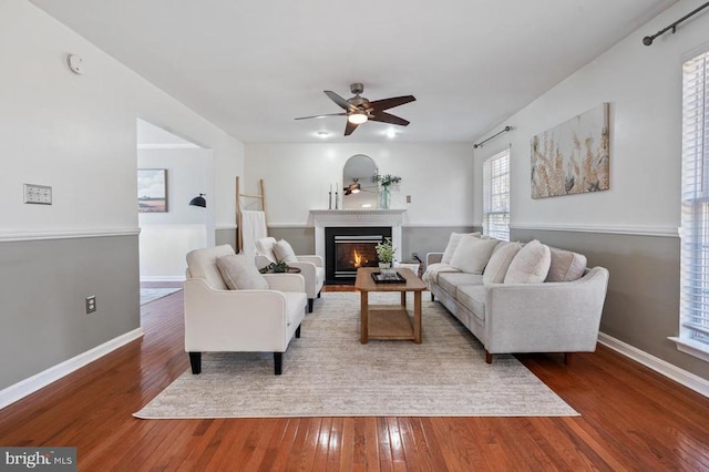 living room with ceiling fan, baseboards, a glass covered fireplace, and hardwood / wood-style flooring