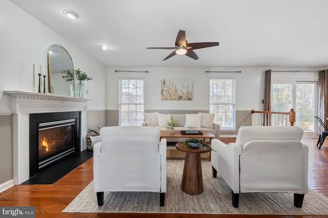 living area featuring a fireplace with flush hearth, ceiling fan, and wood finished floors