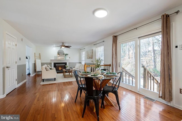 dining space featuring baseboards, visible vents, ceiling fan, a lit fireplace, and hardwood / wood-style flooring