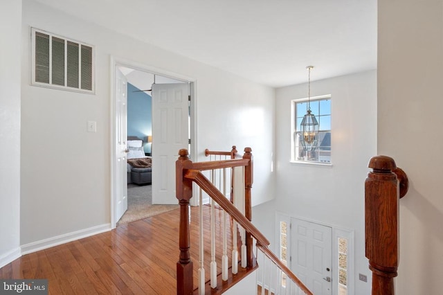 staircase featuring a chandelier, visible vents, baseboards, and hardwood / wood-style floors