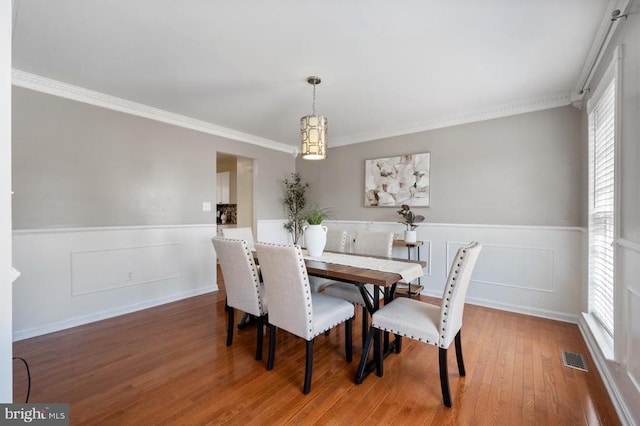 dining room featuring visible vents, wood finished floors, a wainscoted wall, and ornamental molding