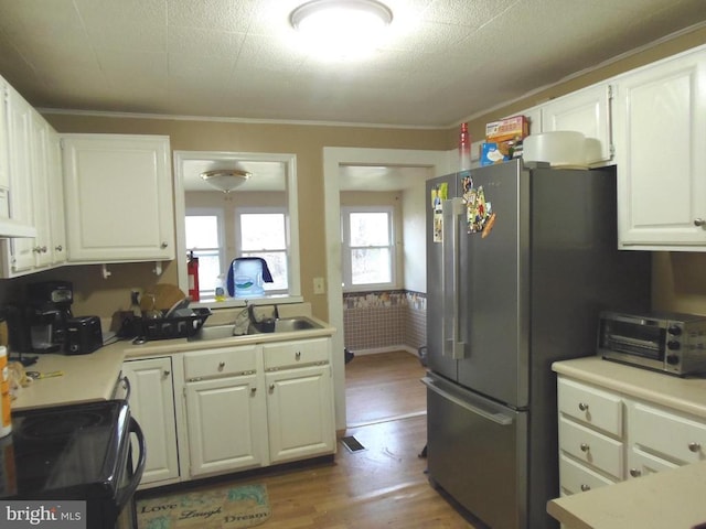 kitchen featuring a sink, wood finished floors, white cabinetry, freestanding refrigerator, and light countertops