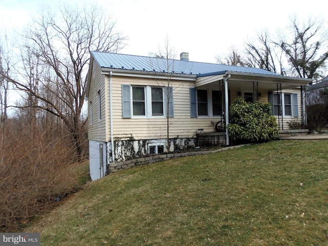 view of front of house featuring metal roof, a chimney, a front lawn, and a porch