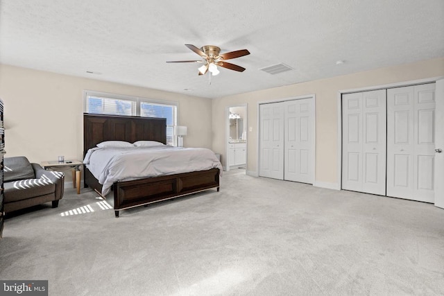 carpeted bedroom featuring multiple closets, visible vents, ceiling fan, a textured ceiling, and baseboards