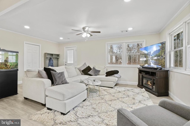 living room featuring a glass covered fireplace, visible vents, crown molding, and wood finished floors